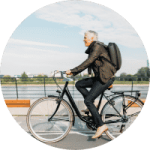 Older gentleman with backpack riding bicycle near water