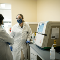 Two Arvinas scientific staff members in face masks standing in front of lab machine